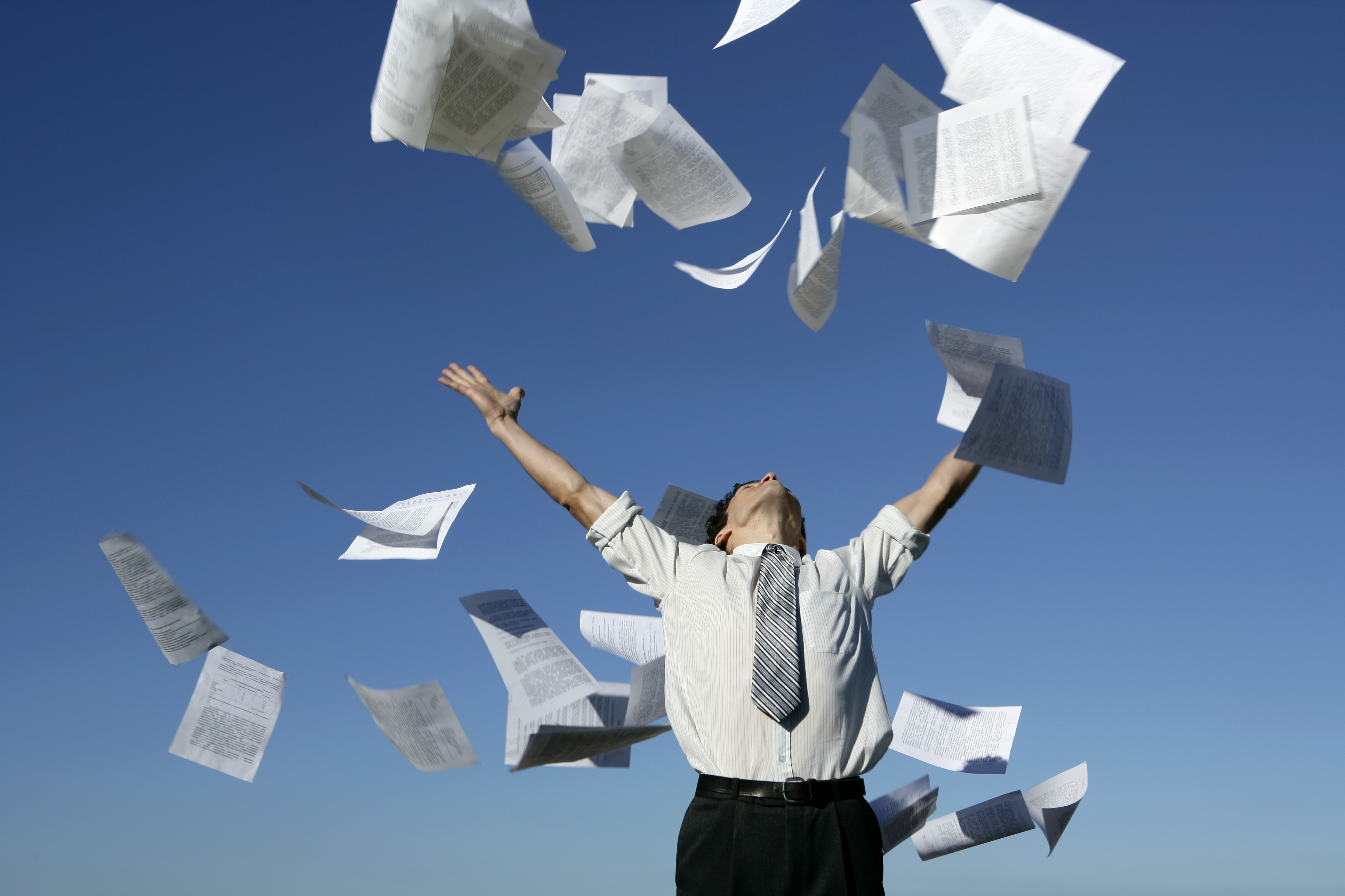 A young businessman throwing away his papers on a blue sky background.