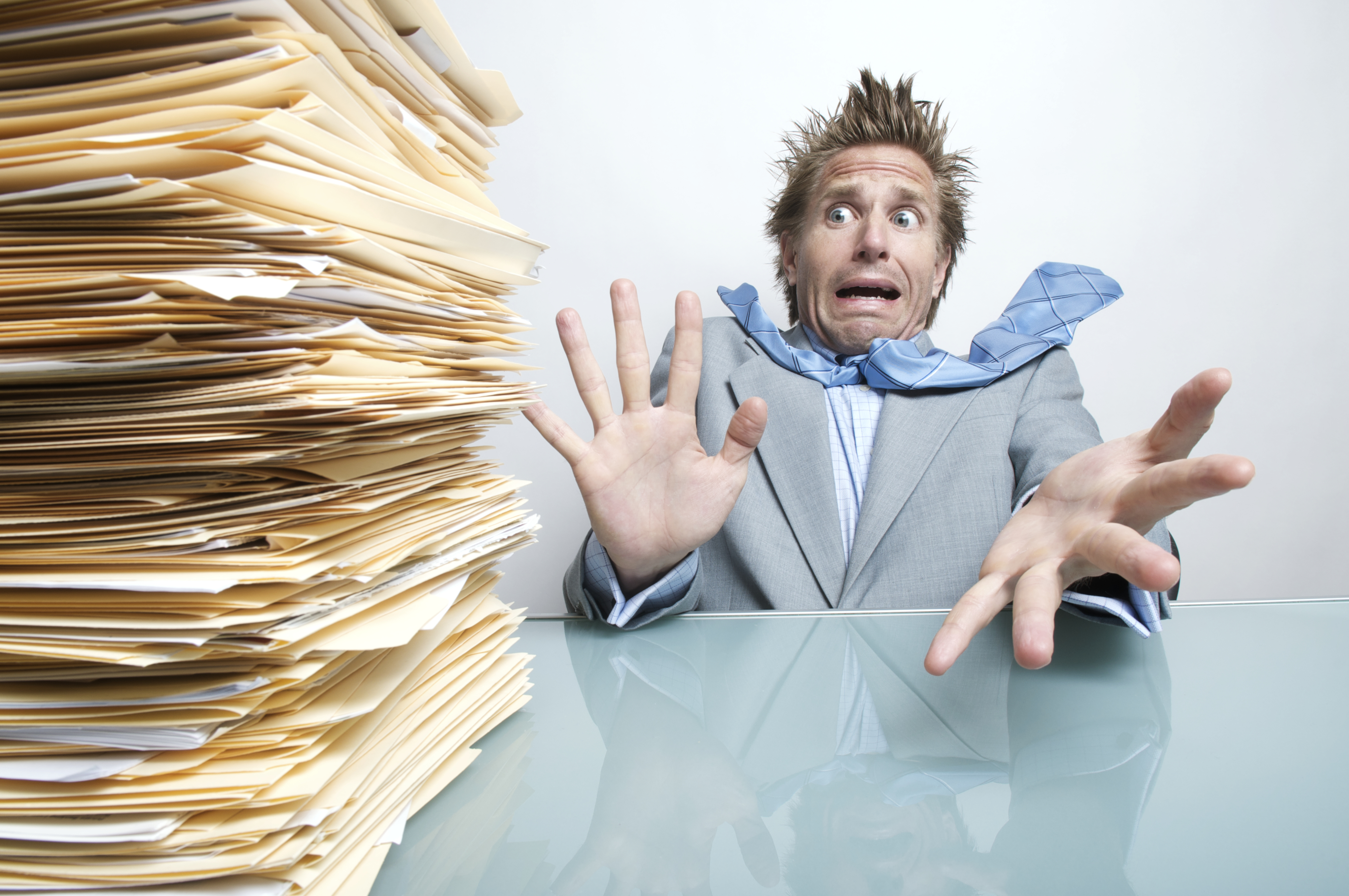 Office worker stresses out at the huge pile of paperwork overflowing in the inbox on his desk