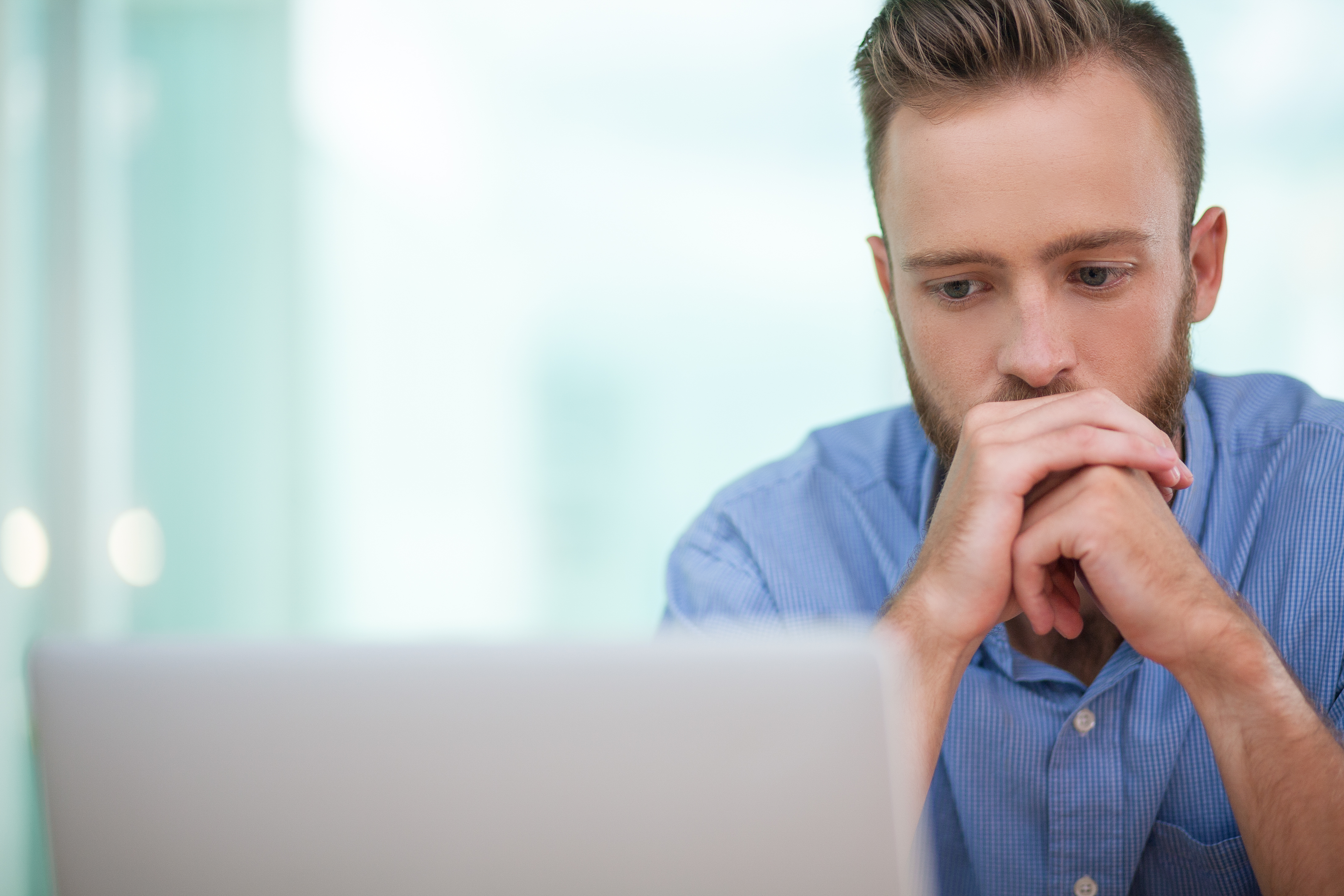 Serious bearded Caucasian businessman looking attentively at laptop screen and trying to solve complicated task